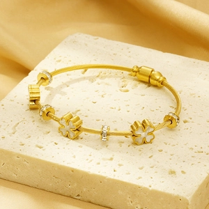 Macro detail of gold-plated braided steel bracelet with shell clover and zircon accents