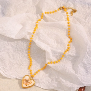 Detailed view of a gold-plated heart locket necklace with yellow beads and dried flowers