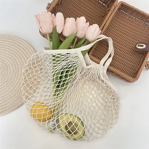 Gros plan du sac en filet de coton tissé avec fleurs et fruits frais dans un décor naturel