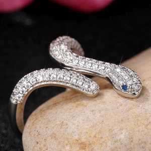 Anillo de serpiente con circonitas y ojos de gema azul sobre piedra de fondo oscuro