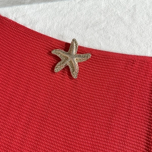 Detailed close-up of a gold starfish ornament on red ribbed fabric swimwear beach set
