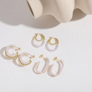 Elegant C-shaped pearl gold earrings set displayed on minimalist white wavy stand