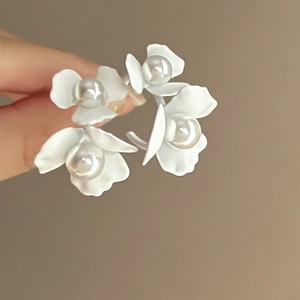 Close-up of white flower earrings with pearls and silver needles in a minimalist style