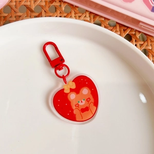 Close-up of a red acrylic heart keychain with a cute brown bear on a white plate