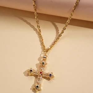 Collier croix dorée vintage avec cristaux colorés sur un fond texturé chaleureux
