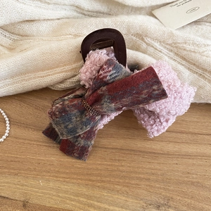 Detail of burgundy plaid and pink faux shearling bow hair claw clip on knit background