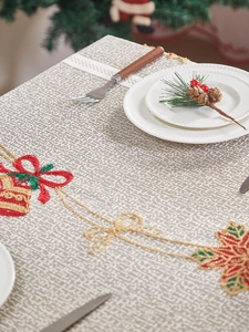 Close-up of festive beige tablecloth featuring red Christmas bell and poinsettia embroidery