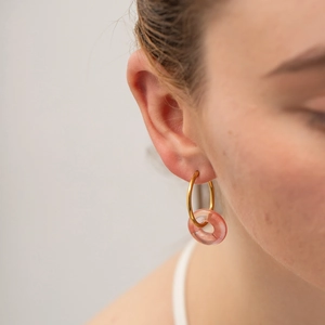 Detail of a gold hoop earring with a pink-orange resin donut charm on a model