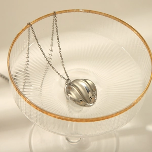 Collier en acier inoxydable argenté avec pendentif vague présenté dans un verre chic