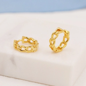 Macro shot of gold Cuban link style chain earrings on a white marble pedestal display