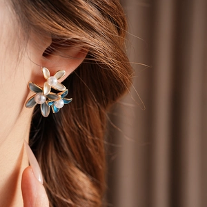 Detailed view of enamel flower earrings with pearls on model, blue petals and gold edge