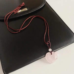 Detail of pink crystal heart pendant on brown woven rope necklace over black leather