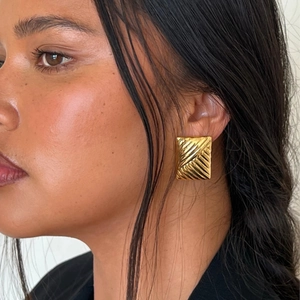 Close-up of gold square earrings with wave texture worn by a model for a chic look