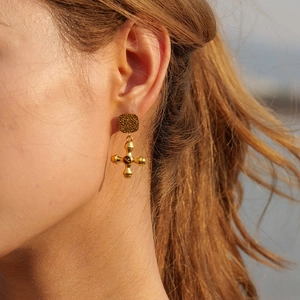 Gros plan d'une boucle d'oreille dorée en acier avec croix et pierre sur le mannequin