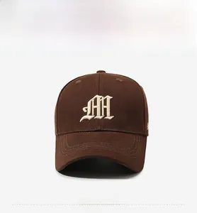 Close-up of brown cotton baseball cap featuring ivory gothic M letter embroidery