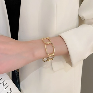 Close-up of a chunky golden chain-link cuff bracelet worn with a white blazer