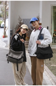 Detail of a large canvas messenger bag shown on models in an urban street setting