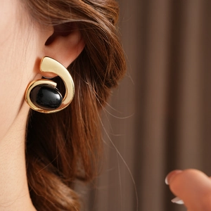 Detailed view of an irregular gold earring set with a polished black oval gemstone