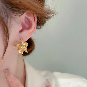 Close-up of golden irregular pleated flower stud earrings worn by a model