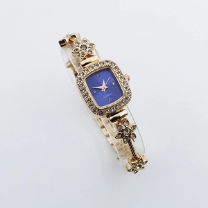 Detail view of gold-toned square watch featuring blue dial and rhinestone flower bracelet