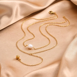 Close-up of double-layer stainless steel chain with pearl and gold ball on silk fabric