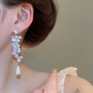 Close-up of light blue flower petal earrings with a water drop pearl on a model