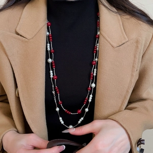 Detail of a layered red bead and faux pearl necklace worn over a black turtleneck sweater