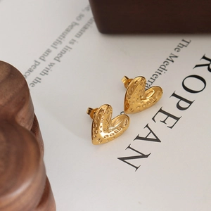 Gold-plated heart stud earrings with irregular hammered texture on aesthetic book background