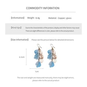 Vue détaillée de boucles d'oreilles à pompons avec pétales en nacre bleue et détails dorés
