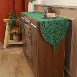 Dark green crochet lace table runner with fringe tassels on vintage wooden cabinet