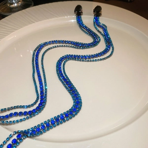 Close-up of long tassel earrings with sparkling blue rhinestones on a white plate