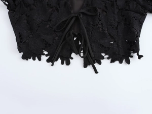 Dettaglio ravvicinato del pizzo nero con trama floreale traforata e nastri decorativi