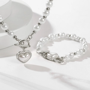 Detail view of pearl jewelry set with heart pendant and OT buckle on neutral backdrop