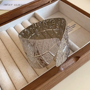 Macro shot of silver wide metal bangle with leaf texture and hinge detail in a gift box