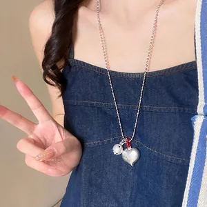 Close-up of vintage heart and bell pendant on bead chain worn by a female model