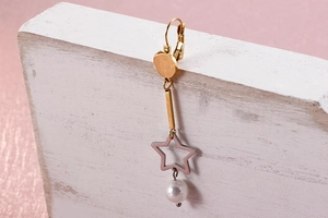 Détail de boucles d'oreilles étoile avec perle blanche sur support en bois naturel