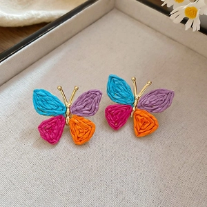 Macro shot of colorful woven butterfly earrings with gold metal details on a tray