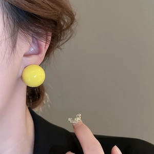 Close-up of a stylish yellow spherical stud earring featuring a smooth polished finish