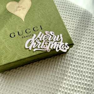 Close-up of Merry Christmas script on embossed green gift box over white texture