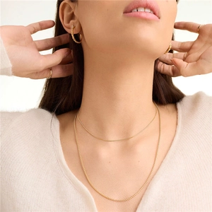 Close-up of layered gold beaded chain necklace and twisted hoop earrings on a model