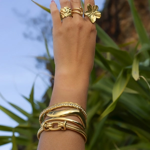 Dettaglio di bracciali e anelli dorati con stelle marine e fiori indossati sul braccio