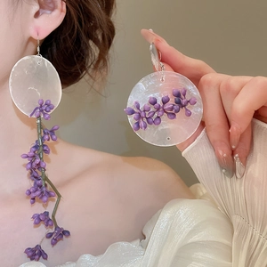 Close-up of purple floral beaded earrings with white shells and long tassels on a model
