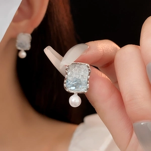 Detailed view of silver square earring with blue crystal and small white pearl hanging