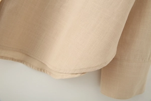 Detailed macro view of the breathable linen texture and stitching on the beige shirt hem