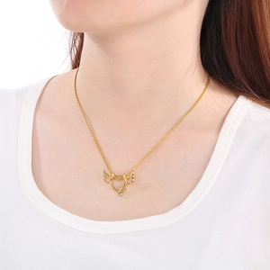 Close-up of a gold heart pendant with angel wings and devil tail on a female model