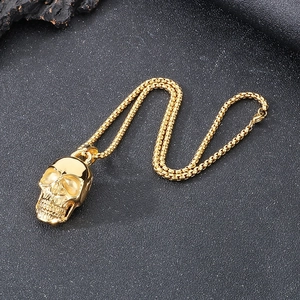 Macro detail of golden skull pendant with matching chain on a dark textured rock surface