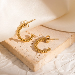 Detail of gold beaded C-shape hoop earrings on textured stone and white silk background