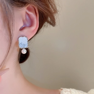 Detail of silver stud earring with ice blue crystal flower and white pearl drop on model