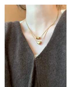 Close-up of double-layer gold titanium necklace with heart and cylinder pendants