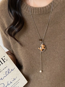 Detail of wooden horse pendant pearl necklace worn on a brown knit sweater
